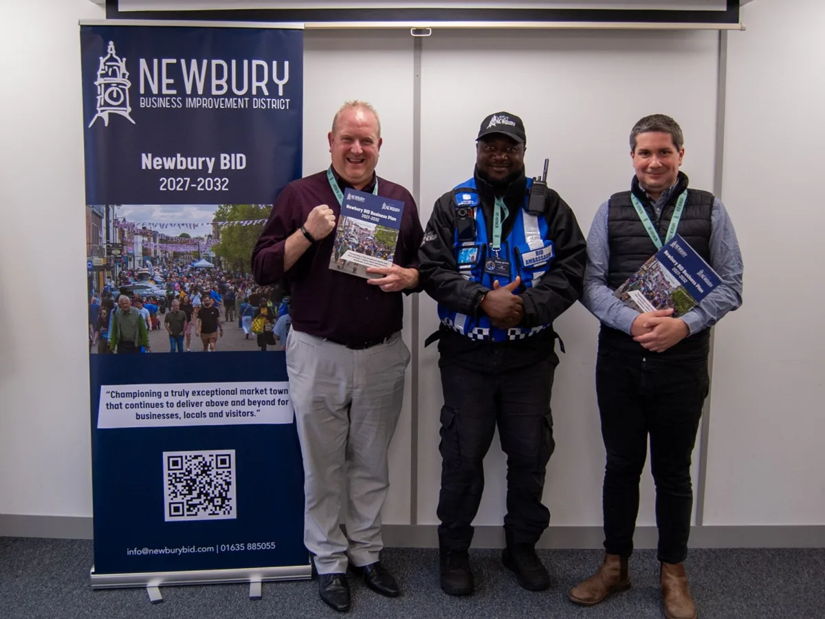Newbury BID's 2027 to 2032 business plan, held up beside the BID's banner, with a BID Ambassador in the centre